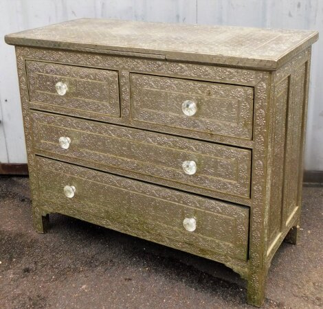 An Eastern style chest of drawers, with inset silver coloured panels, heavily embossed with flowers, with two short and two long drawers, and shelf pull out centre section, imitation crystal handles, 89cm high, 107cm wide, 50cm deep.