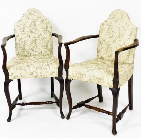 A pair of early 20thC armchairs, each with a shield shaped back on carved oak arms on a H base, upholstered in a cream floral upholstery, 100cm high, 55cm wide, 50cm deep.