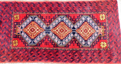 A middle Eastern style rug, with three layered border and three central medallions, on a red and blue ground with white tassel ends, 169cm x 85cm.