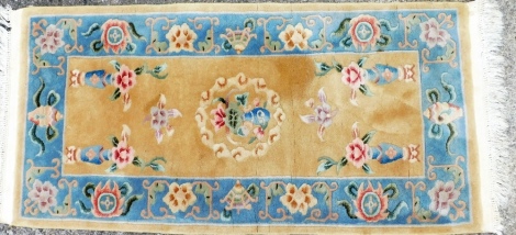 A Chinese wool cut rug, on a yellow ground with blue floral vase borders, with cream sculptured tassel ends, 138cm x 69cm.