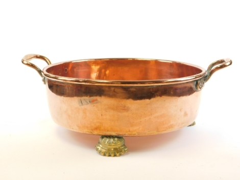 A Victorian copper bowl, with two loop handles on three claw feet, stamped, 20cm high, 60cm wide.