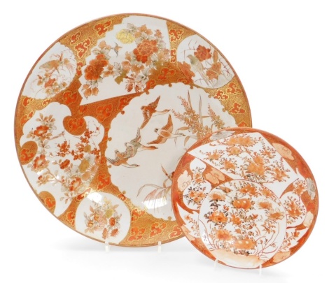 Two Japanese Kutani porcelain dishes, the larger saucer dish decorated with shaped panels of birds in flight, flowering branches, etc., on a red and gold ground, marked Dai Nihon Kutani sei, 36.5cm diameter, and a smaller similar saucer dish marked Kutani