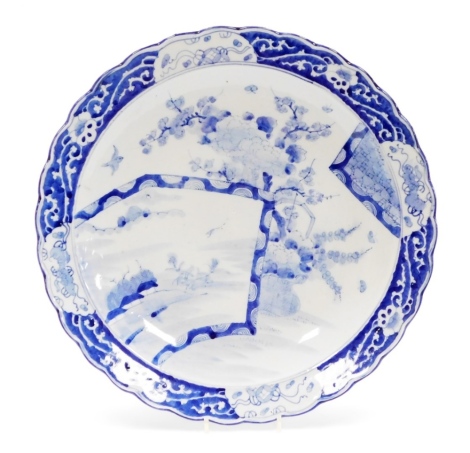 A Japanese blue and white porcelain charger, decorated with a fan shaped panel with birds, prunus, flowers, etc., within a scrolling border, Meiji period, 45.5cm diameter.