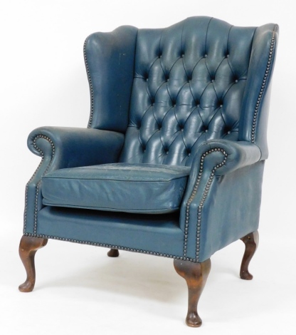 A late 19thC Chesterfield style wing back armchair, in blue leather upholstery with button back and borders, on mahogany splay legs, 107cm high, 77cm wide, 63cm deep.