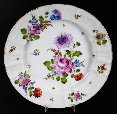 An 18thC Continental porcelain plate, moulded, shaped and decorated with large flowers and groups within a gilt rim, crossed sword mark in underglaze blue, c1780, 24cm diameter.