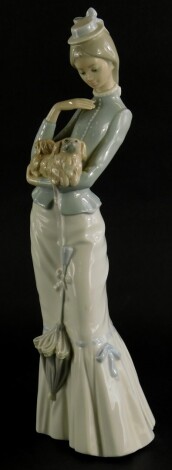 A Lladro porcelain figure of a tall lady, holding a Pekingese dog whilst holding a parasol, 38cm high.