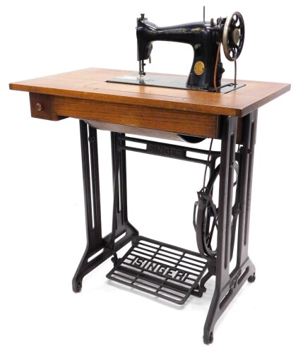 A Singer treadle sewing machine table, the fold-and-reveal machine numbered ED042387, on an oak and cast iron treadle base, 94cm high, 79cm wide.