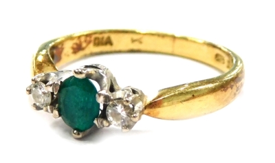 An 18ct gold emerald and diamond set dress ring, the central oval cut emerald in six claw setting, flanked by two tiny diamonds, in white gold on a yellow metal band, ring size L, 3.1g all in.