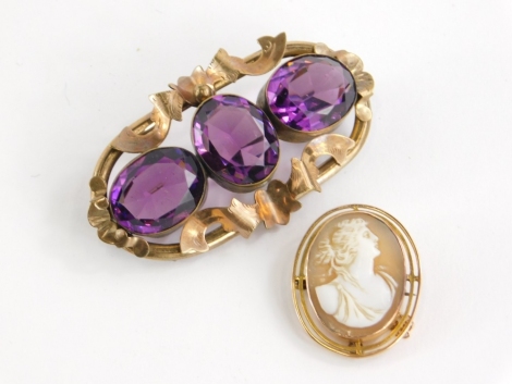 Two brooches, to include a cameo brooch with two layered oval surround, gold coloured but unmarked, 3cm x 2cm, and an oval brooch set with three purple paste stones in a rolled gold scroll border, 6cm wide.