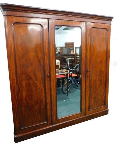 A Victorian figured mahogany triple wardrobe, with a moulded cornice above a central mirror, flanked by two panelled doors, enclosing sliding trays, drawers and recesses, on a plinth, 207cm high, 197cm wide.