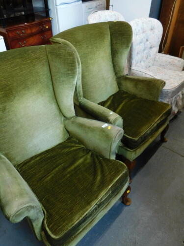 A pair of wing back armchairs, in green velvet upholstery, on pad feet, and a pair of button back armchairs, in floral fabric. The upholstery in this lot does not comply with the 1988 (Fire & Fire Furnishing) Regulations, unless sold to a known exporter o