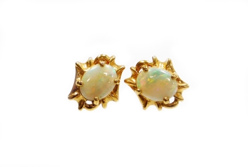 A pair of opal stud earrings, with oval opal in four claw setting, surrounded by abstract twist design bordering, on stem back with butterfly backs, yellow metal unmarked, the back stamped 750, each earring head 1cm high, 5.5g all in.