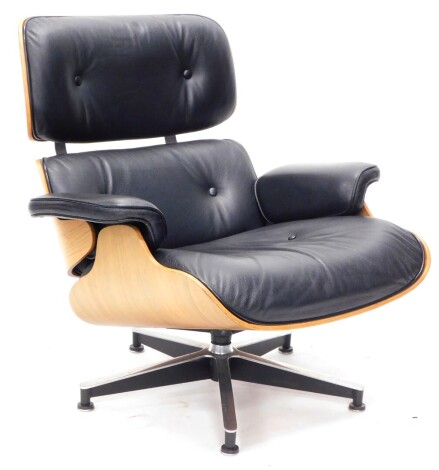 A walnut and black leather swivel armchair in the manner of Charles and Ray Eames, with a padded back, arm rests and seat, and a star shaped metal base.