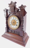 A late 19thC Ansonia Clock Company stained pine cased mantel clock, circular brass dial with enamel chapter ring bearing Roman numerals, eight day movement with coil strike, the case carved with acanthus leaves and palmettes, with turned columns, raised o