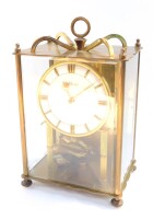 A Wilmac brass 400 day anniversary clock, circular silvered dial, the movement raised on fluted columns, case with bevelled glass front and side panels, raised on ball feet, 26cm high, 16cm wide, 12cm deep.