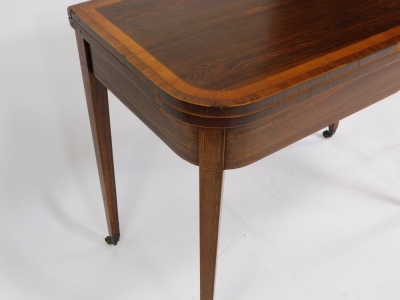 A George III rosewood and satinwood cross banded demi lune fold over card table, raised on tapering square legs, brass capped on castors, 73cm high, 91cm wide, 46.5cm deep. - 4