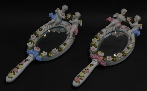 A pair of continental Meissen style porcelain hand mirrors, surmounted with cherubs, and encrusted with roses, inset oval bevelled glass, 27.5cm high.