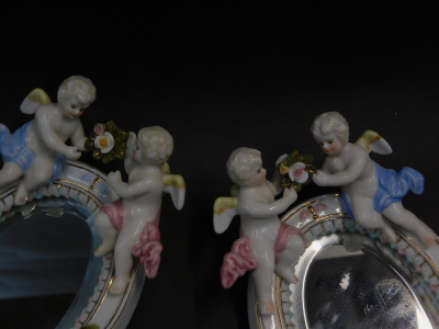 A pair of continental Meissen style porcelain hand mirrors, surmounted with cherubs, and encrusted with roses, inset oval bevelled glass, 27.5cm high. - 2