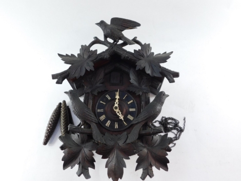 An early 20thC Black Forest cuckoo clock, heavily carved and surmounted by bird and flowers above the cuckoo and door with a 14cm diameter Roman numeric dial in a heavily carved case, weight driven, 42cm high.