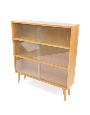 A vintage lightwood bookcase, of rectangular form, with sliding glass doors, on tapering circular feet, 100cm high, 85cm wide, 23cm deep.