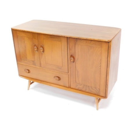 A 20thC Ercol light elm side cabinet, of oblong form, with two cupboards above drawer flanked by a side further cupboard on circular tapering legs, 82cm high, 113cm wide, 46cm deep.