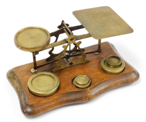 A set of early 20thC brass postal scales, on a wooden base with inscription postage rates for letters with an assortment of five weights on shaped mahogany base, 15cm high, 26cm wide, 14cm deep.