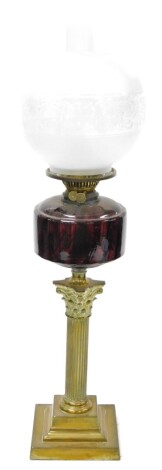 A late 19thC brass oil lamp, with a shade and reservoir, on a cranberry glass dome, on brass Corinthian column stepped base, 74cm high.