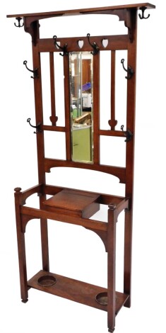 An Art Nouveau walnut hall stand, with top shelf and hanging hooks with central rectangular mirrored panel, with spade carving, central glove box and drip trays, 190cm high, 69cm wide, 29cm deep.