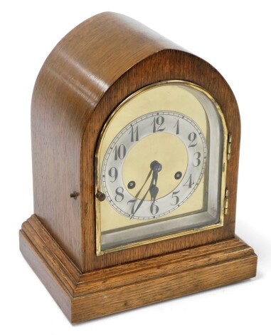 An early 20thC oak cased mantel clock, with arched central brass dial, on a staggered base, 29cm high, 23cm wide, 17cm deep.