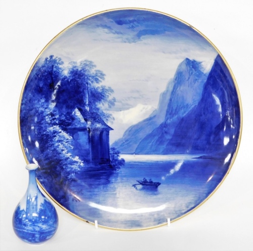 Two items of blue and white pottery, to include an Italian blue and white charger depicting mountain and lake scene, signed and stamped to reverse, with gilt border, 31cm wide, and a blue and white bud vase depicting a Cathedral 11cm high. (2, AF)