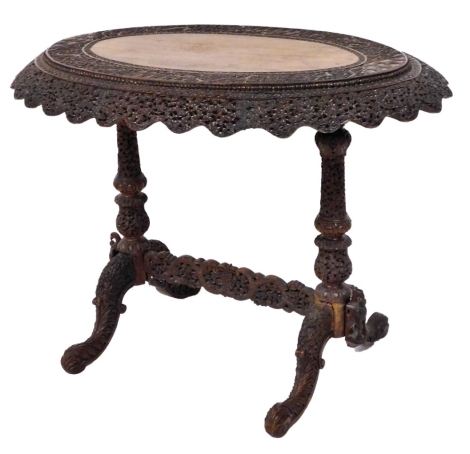 An Burmese carved hardwood side table, the oval top with figures, buildings, leaves, etc, on end supports, with stretcher, 80cm high, 100cm wide, 73cm deep.