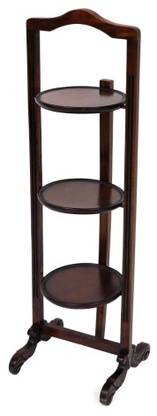 A mahogany three tier cake stand, on scroll feet, 98cm high.