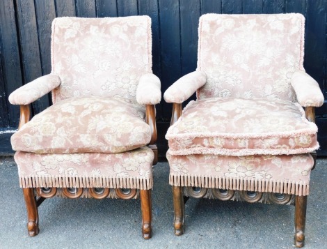 A pair of 1920s arm chairs, each with mahogany scroll arms on cabriole legs, later upholstered in pink floral upholstery with tassel boarders, 90cm high, 66cm wide, 54cm deep.