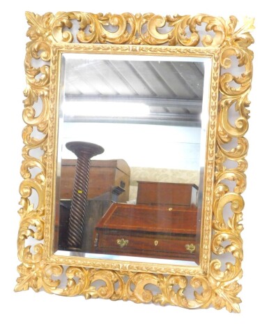 A late 18th/early 19thC giltwood wall mirror, the frame carved with scrolls, leaves, etc., surrounding a later bevelled mirror plate, 87cm high, 70cm wide.