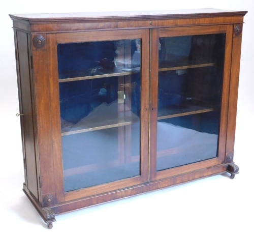 An early 19thC mahogany freestanding library bookcase, the top with a moulded crest above two glazed doors, each flanked by roundel's, the reverse with two panelled doors, and with further side doors to each narrow end, on leaf carved end supports with ca