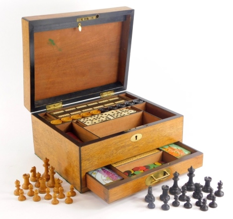 A 19thC oak games box or compendium, the hinged lid with a vacant oval cartouche enclosing bone and ebonised dominoes, draughts, chess set, etc., 33cm wide.