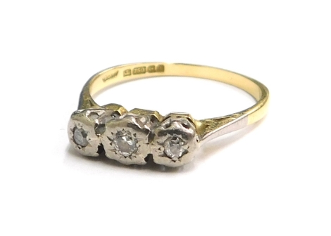 An 18ct gold three stone diamond ring, the three diamonds in rub over setting, in platinum setting, on a yellow metal band, ring size L, 2.4g all in.