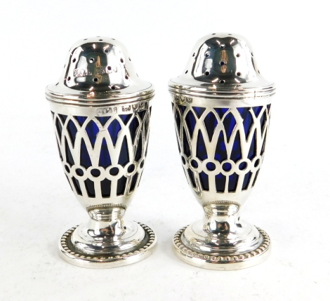 A pair of Victorian pepper pots, each with a pierced body revealing a blue glass liner, on a pedestal base with beaded border, London 1898, weighable silver 1½oz, 7cm high. (2)