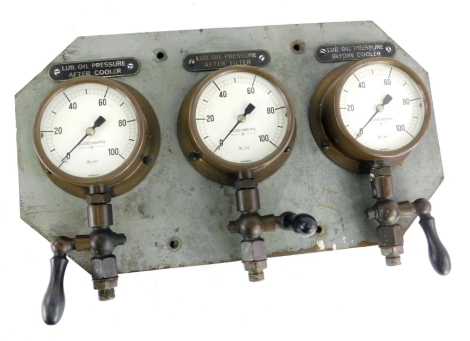 A set of three Budenberg brass pressure gauges, mounted onto metal, with a metal backing for Lub Oil Pressure, after cooler, after filter and before filter, 46cm wide.