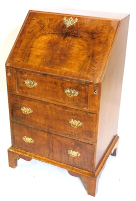 A walnut bureau, the figured fall with a pierced brass escutcheon enclosing a fitted interior, above three drawers on bracket feet, 58cm wide.