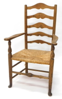 An early 19thC ash and elm country made ladder back chair, with shaped arms, and a rush seat on turned legs with pad feet.