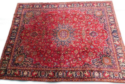 A large Persian Meshed type carpet, with a central medallion, surrounded by an elaborate design to the floral red ground, with blue spandrels, one wide and three narrow borders, 373cm x 280cm.