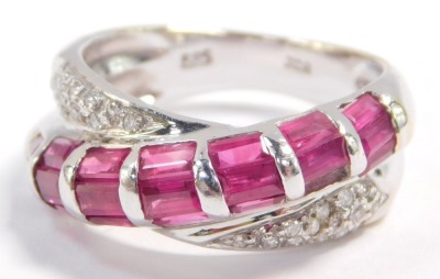 A ruby and diamond crossover ring, set with twenty one baguette cut rubies in white metal, stamped 585, size M, 4.7g.