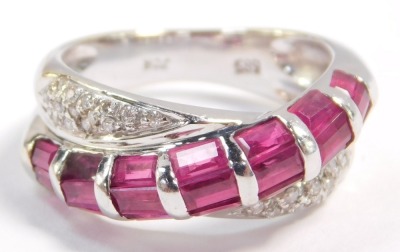 A ruby and diamond crossover ring, set with twenty one baguette cut rubies in white metal, stamped 585, size M, 4.7g. - 2