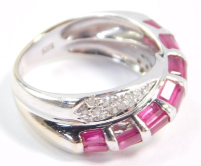 A ruby and diamond crossover ring, set with twenty one baguette cut rubies in white metal, stamped 585, size M, 4.7g. - 4