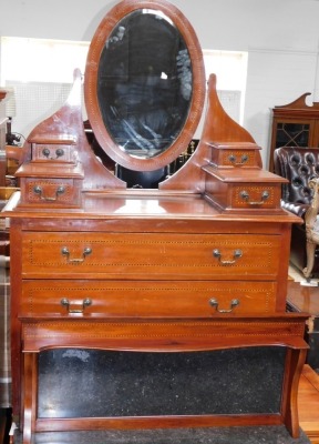 An Edwardian mahogany three piece bedroom suite, comprising wardrobe with oval bevelled mirror plate and a drawer, 130cm wide, a dressing table with oval bevelled plate, four trinket drawers and two long drawers, on brass castors, 101cm wide, and a washst - 3