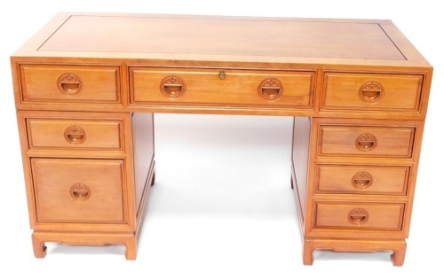 An Oriental hardwood desk, with a paneled top above an arrangement of nine drawers, each with recessed carved handles, on bracket feet, 79cm high, 137cm wide.