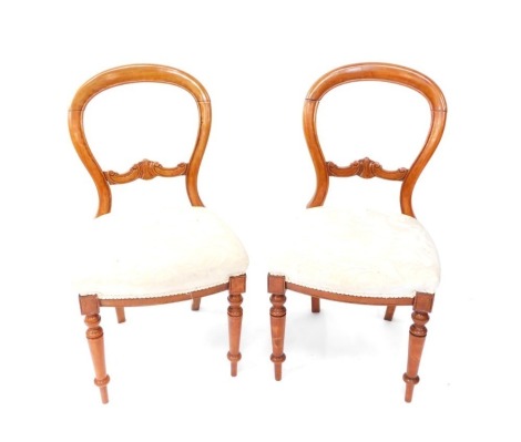 A pair of Victorian balloon back chairs, each with heavily carved horizontal scroll splats, and overstuffed seats in cream material, on turned front legs, 86cm high. (2)