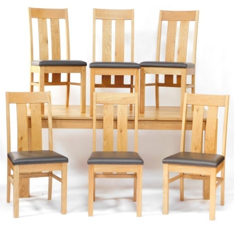 A modern light oak extending dining table, on square section legs, with extension leaves to each end, with a set of six dining chairs, each with rail shaped backs and black PVC seats.