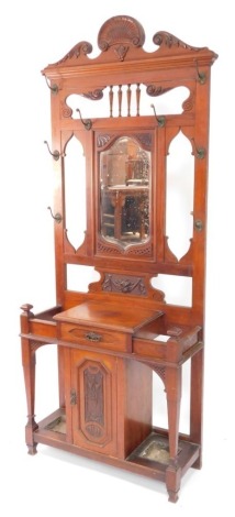 A late Victorian walnut hall stand, the shaped crest carved with a shell, leaves, etc., above a bevelled plate surrounded by cast brass hooks, etc., the base with a frieze drawer above a carved panelled door flanked by recesses for umbrellas, each with a 